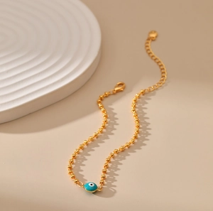 Detalle de pulsera de cuentas doradas con amuleto de ojo azul y cadena ajustable