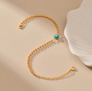 Detalle de pulsera de cuentas doradas con dije de ojo turco azul y cierre de mosquetón
