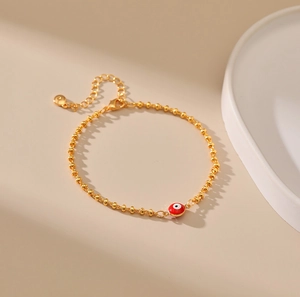 Detalle de la pulsera de cuentas doradas con amuleto de ojo rojo esmaltado y cierre
