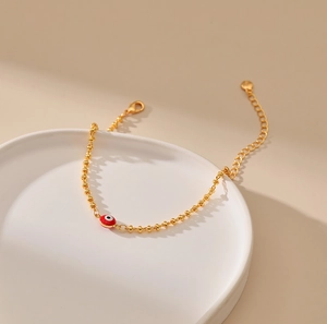 Detalle de pulsera de cuentas doradas con dije de ojo turco rojo y cierre de langosta