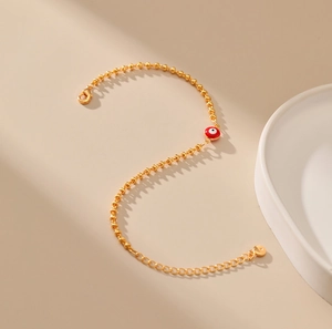 Detalle de la pulsera de cadena de bolas doradas con dije de ojo esmaltado rojo