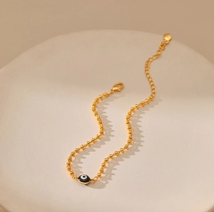 Detalle de pulsera de cuentas doradas con dije de ojo turco y cierre de langosta ajustable