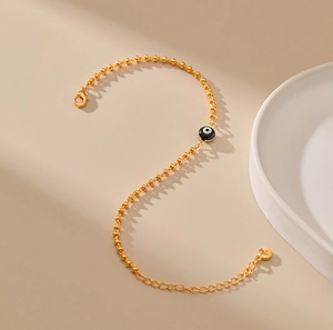 Detalle de pulsera dorada de cuentas con dije de ojo turco y cierre de mosquetón