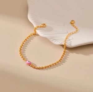 Detalle de pulsera de cuentas doradas con dije de ojo turco rosa y cadena de corazón
