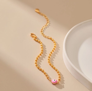 Detalle de pulsera de cuentas doradas con ojo de esmalte rosa y cierre ajustable