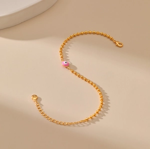 Detalle de pulsera de cuentas doradas con dije de ojo esmaltado rosa y cadena de extensión