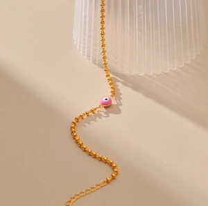 Primer plano de un dije de ojo turco rosa en una pulsera de cadena de cuentas doradas