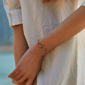 18K gold plated thin chain bracelet with blue evil eye charms worn by a model in sunlight