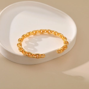 Detailed close-up of golden O-chain open cuff bracelet on white ceramic display plate