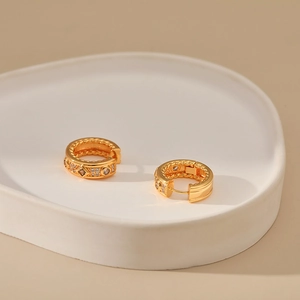 Klassische französische Retro-Goldohrringe mit Zirkonia auf einer weißen Keramikschale