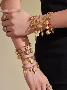Detail of bohemian gold seashell, fish and leaf charms on multi-layered bracelets