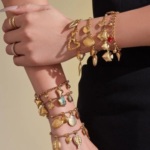 Golden stainless steel bracelet with shell, fish and heart charms on woman's wrist
