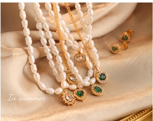 Vue détaillée du collier en perles baroques avec pendentif cœur émeraude sur tissu soyeux