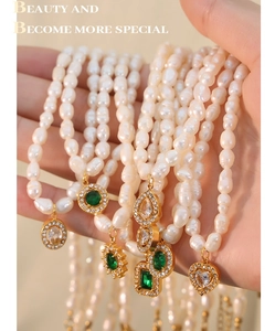 Gros plan d'un collier de perles baroques avec pendentif cœur doré et gemmes vertes