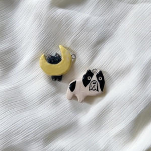 Detail of handcrafted ceramic cat on moon and black and white dog charms with glazed finish