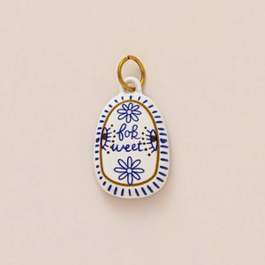 Detail of white ceramic oval pendant with blue floral patterns and for sweet engraving