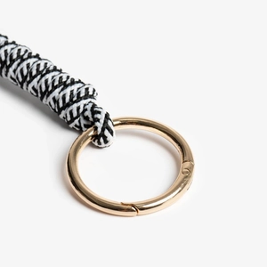 Close-up of woven black and white cord keychain with a polished golden spring ring clasp
