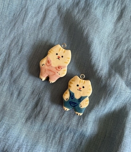 Detail shot of hand-painted ceramic cat pendants in pink and blue outfits on blue fabric