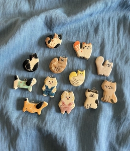 Detailed flat lay of twelve diverse hand-painted ceramic cat and dog charms on blue fabric