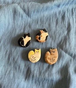 Detail view of four hand-painted ceramic cat pendants with metal loops on blue linen