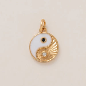 Dettaglio macro di un ciondolo Yin Yang placcato oro 18K con smalto bianco e cristalli
