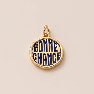 Detailed macro view of gold round pendant with blue enamel and Bonne Chance engraving
