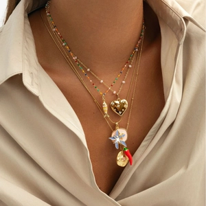 Gelaagde gouden ketting met hart-, vis- en bloemhangers gedragen door een vrouwelijk model