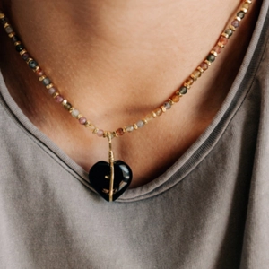 Detail van kleurrijke kralenketting met een zwarte hartvormige hanger en gouddraad
