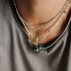 Detail van een gelaagde roestvrijstalen hartketting met blauwe en gele zirkoonhangers