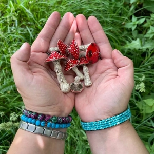 Detail of red and white mushroom pendants with metal loops held in hand against grass