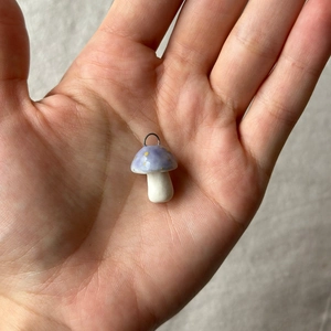 Makroaufnahme eines lila Pilzanhängers mit gelben Punkten und Silberring auf der Hand