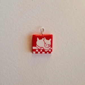 Détail d'un pendentif carré rouge avec deux chats blancs de dessin animé et crochet argent