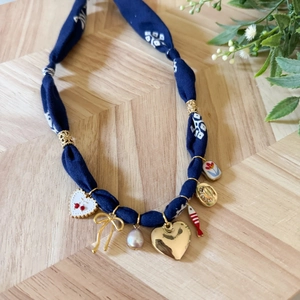 Dettaglio collana in tessuto floreale blu con ciondoli a cuore e perle su sfondo in legno