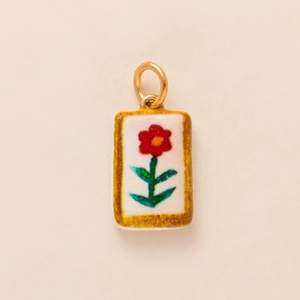 Detail of a rectangular gold flower pendant with white background and red floral pattern