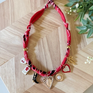 Collana in tessuto rosso floreale con ciondoli bohémien e perle su fondo in legno naturale