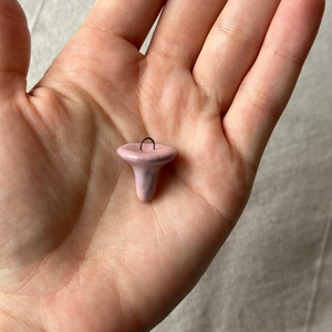 Detailaufnahme eines kleinen rosa Pilzanhängers mit schwarzem Ring in der Hand