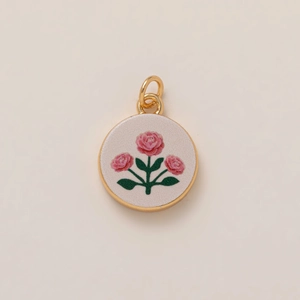 Round golden floral pendant featuring pink rose embroidery on textured fabric