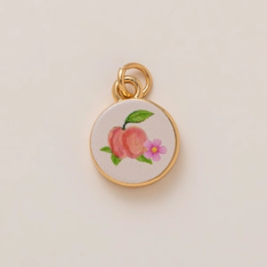 Cute round golden pendant featuring a peach and pink flower design on a white base