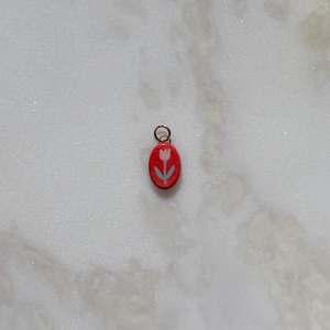 Macro shot of an oval red pendant featuring hand-painted pink tulip and golden metal loop