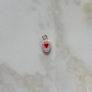 Detailed view of an oval pendant with a red heart design and pink grid patterns on white base