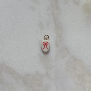 Detail of a mini white oval pendant featuring a red bow tie pattern for DIY jewelry
