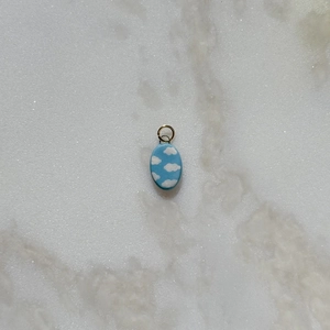 Close-up of oval sky blue pendant with white cloud pattern on a marble surface