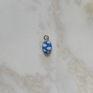 Oval stainless steel pendant with blue sky cloud pattern on white marble surface