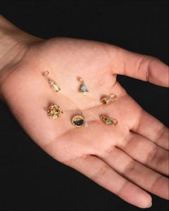 Set di sei mini ciondoli dorati con zirconi colorati tenuti nel palmo della mano