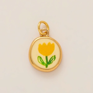 Detail eines goldenen Anhängers mit gelber Tulpenstickerei auf cremefarbenem Hintergrund