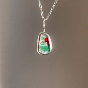 Detail van een 18K gouden hanger met handbeschilderde bloemenkeramiek en een fijne ketting