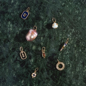 Detailed macro view of assorted 14k gold charms with baroque pearls and blue enamel gems