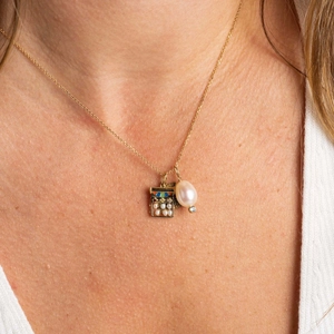 Close-up of gold necklace featuring abacus, teardrop pearl, and blue gem charms