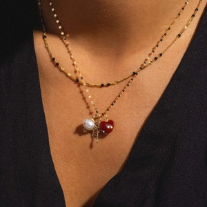 Close-up of layered gold chains featuring a white pearl and red heart pendant