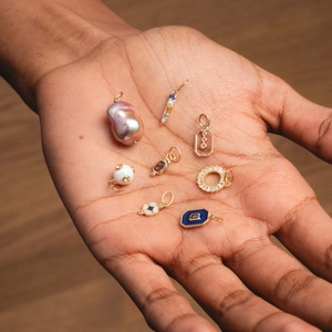 Detailed hand-held view of 14K gold pearl, opal, and enamel jewelry pendants